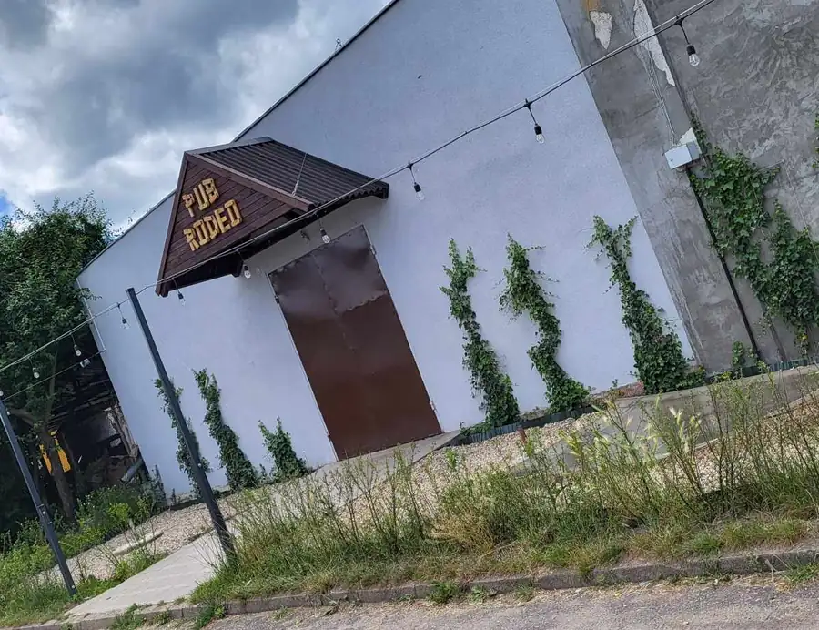 Biały budynek z drewnianym daszkiem i zielenią